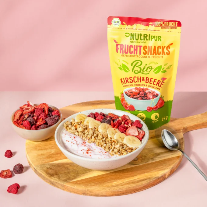 Hier ist ein Bild mit dem Nutripur Kirsch-Beeren-Mix mit Müsli und Joghurt in einer Müslischale. Im Hintergrund ist die Verpackung abgebildet.