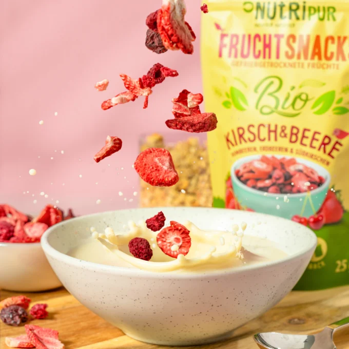 Hier ist ein Bild mit gefriergetrocknetem Bio-Früchte-Mix Kirschen und Beeren in einer Schale mit Joghurt. Im Hintergrund ist die Verpackung abgebildet